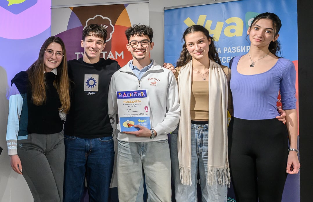 Five young people smiling and posing, one holding a colorful award certificate in front of banners.