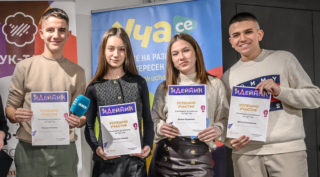 Four smiling young people holding certificates of participation at an event with colorful banners behind.