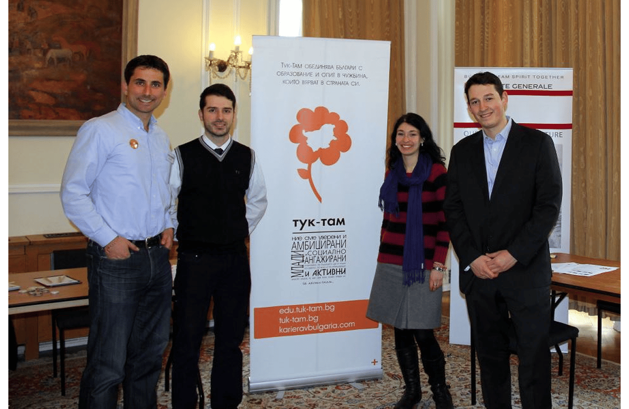 Four people standing beside a banner with Bulgarian text in a formal room.