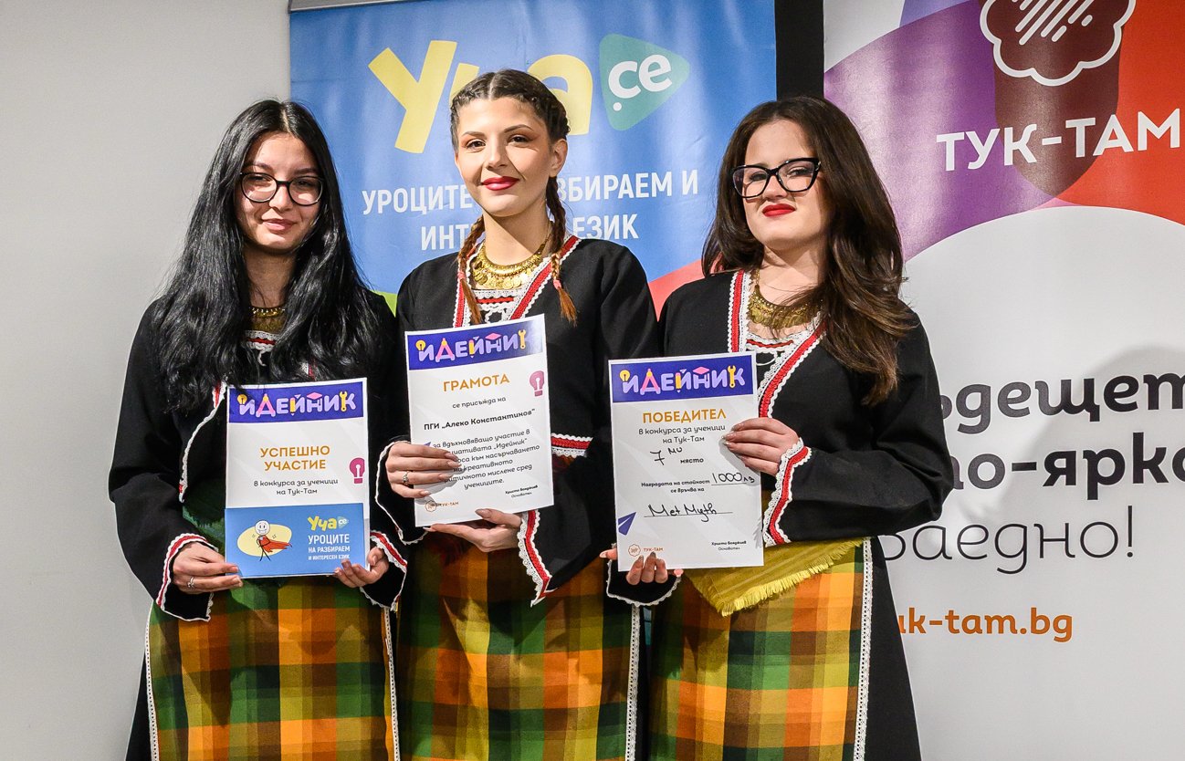 Three women in traditional attire holding certificates and smiling at an award event.