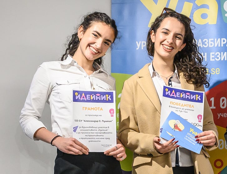 Two young women smiling and holding award certificates at a creative competition event.