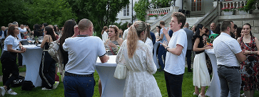 People socializing near tall white cocktail tables at an outdoor garden party.