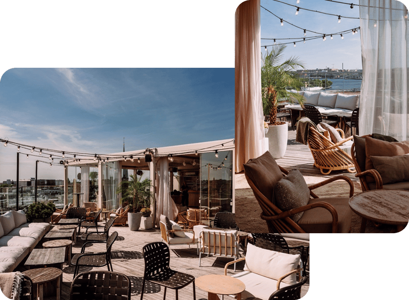 Open-air rooftop lounge with wicker chairs, cushioned sofas, string lights, and a view of the city and water.